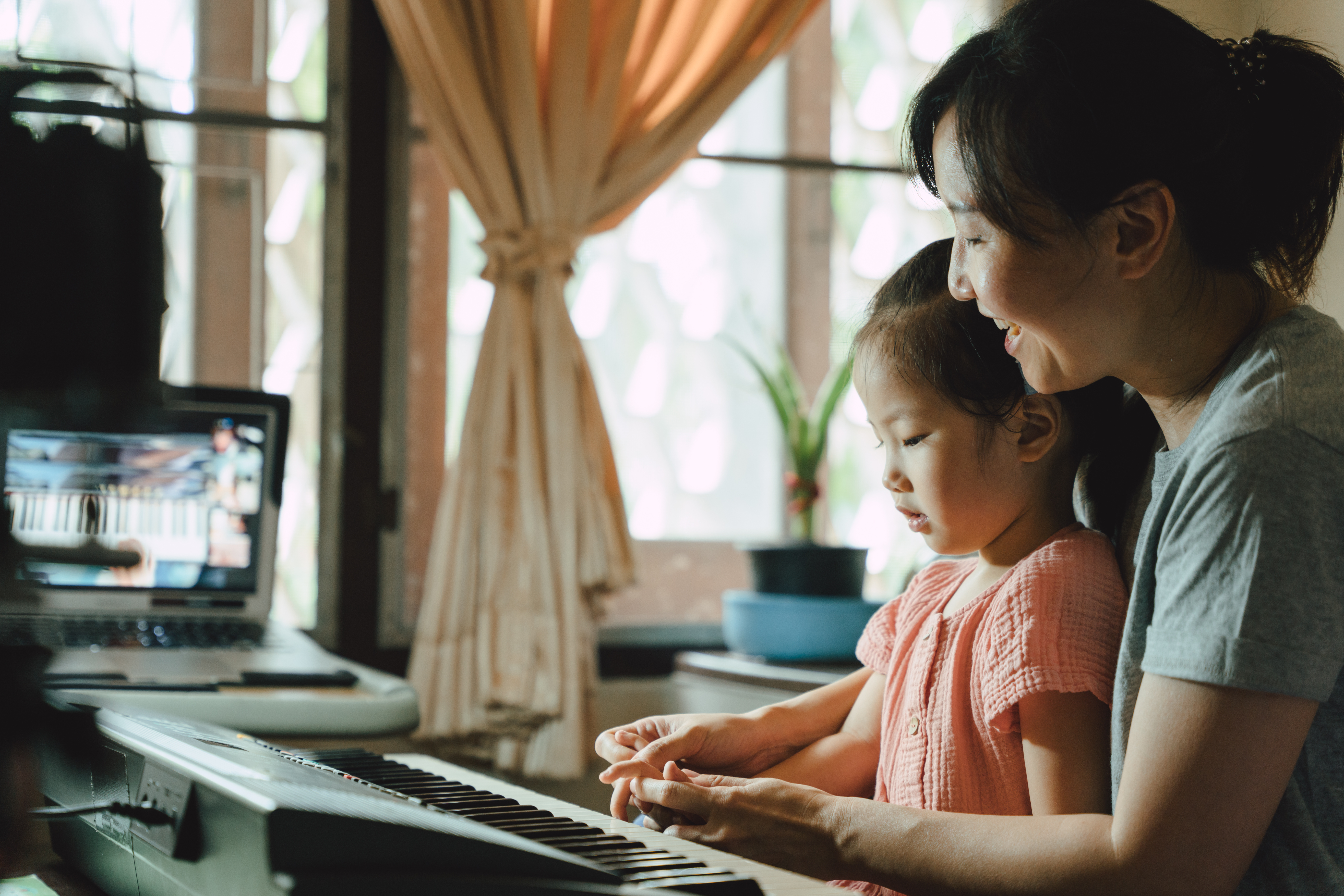 Asian mother helping and teaching daughter to play the piano dur